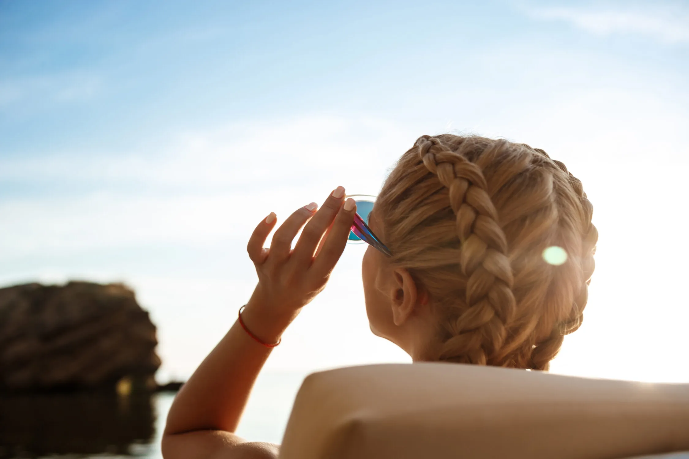 Bellissima ragazza bionda con occhiali da sole che prende il sole vicino al mare. Spazio per il testo.