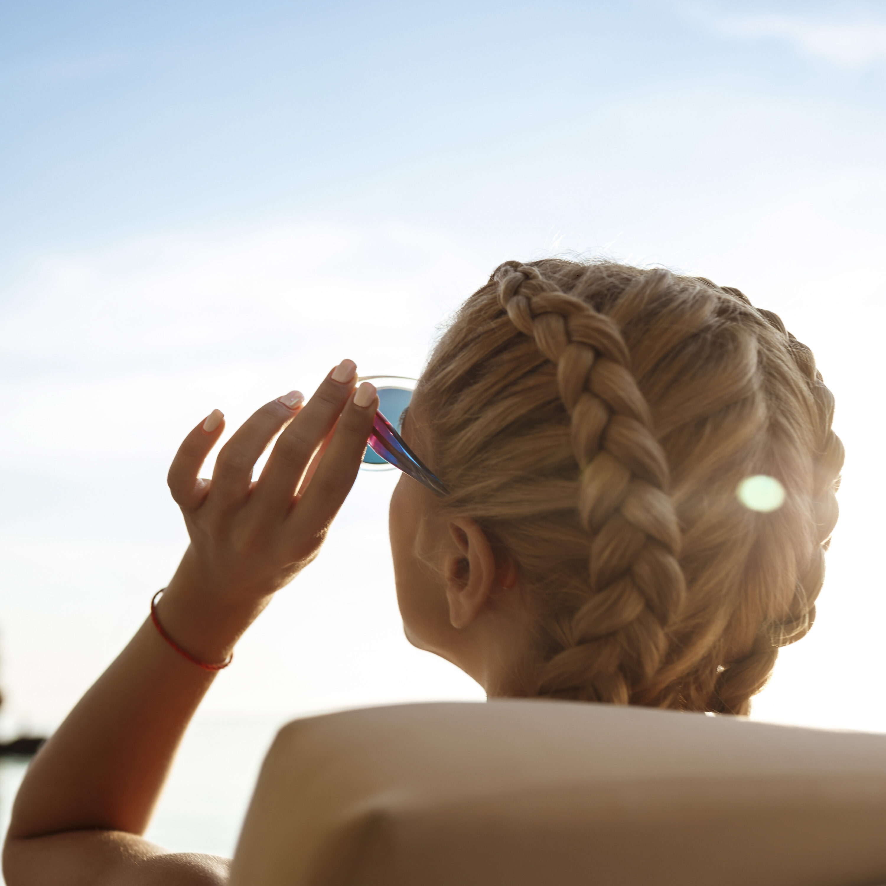 Bellissima ragazza bionda con occhiali da sole che prende il sole vicino al mare. Spazio per il testo.